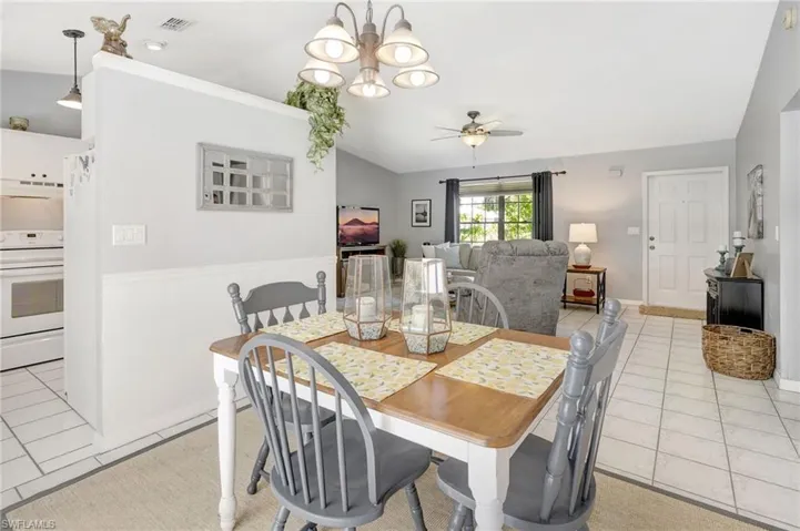 Dining space with ceiling fan with notable chandelier, vaulted ceiling, and light tile patterned flooring