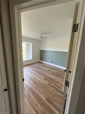 Empty room with light wood-type flooring, wainscoting, and a ceiling fan
