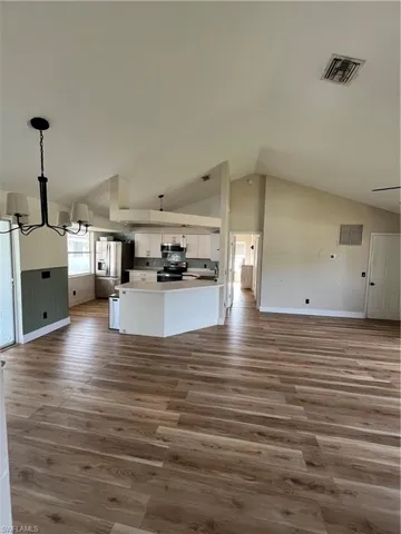 Unfurnished living room featuring a chandelier, dark wood finished floors, and vaulted ceiling