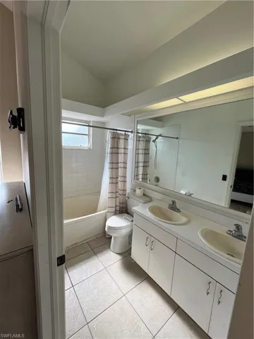 Full bath featuring double vanity, shower / bath combo with shower curtain, light tile patterned flooring, and lofted ceiling