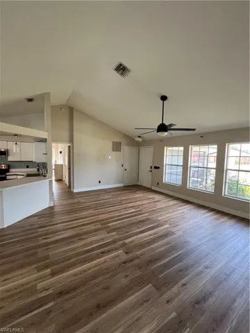 Unfurnished living room with dark wood-type flooring, a ceiling fan, and high vaulted ceiling