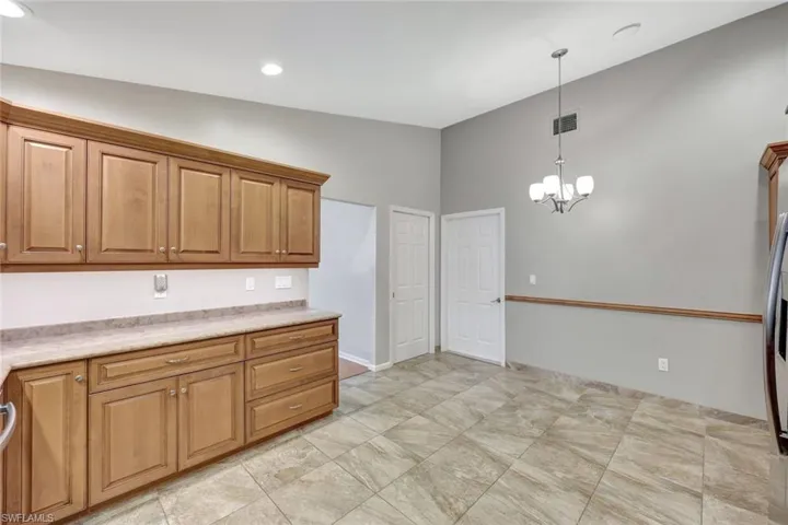Kitchen featuring light countertops, pendant lighting, a chandelier, brown cabinetry, and recessed lighting