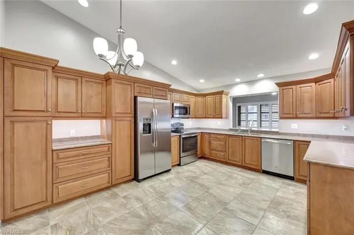 Kitchen with stainless steel appliances, lofted ceiling, brown cabinetry, a chandelier, and recessed lighting