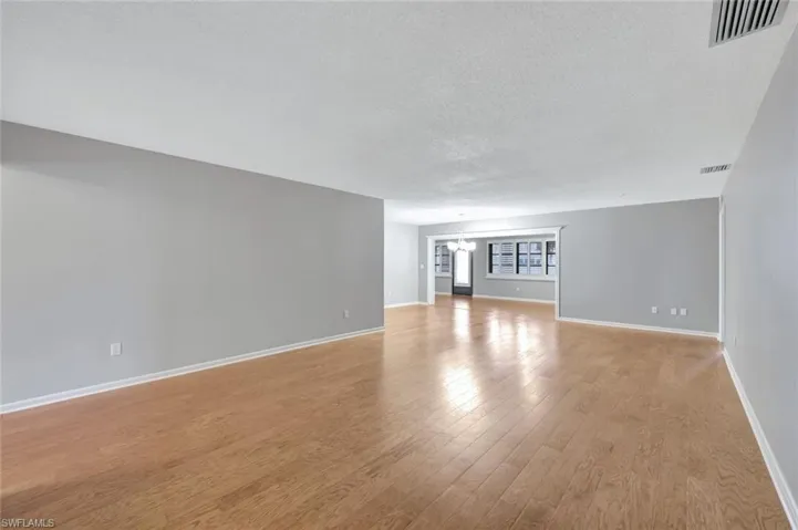 Unfurnished living room featuring a chandelier, light wood-type flooring, and a textured ceiling