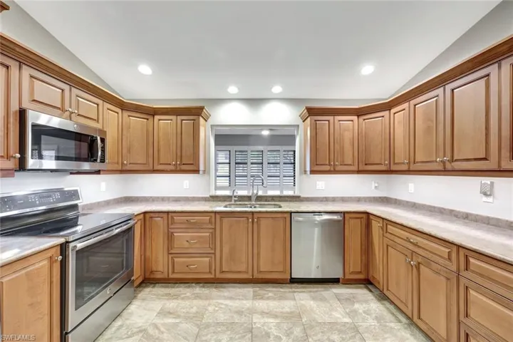 Kitchen with stainless steel appliances, vaulted ceiling, light countertops, brown cabinets, and recessed lighting
