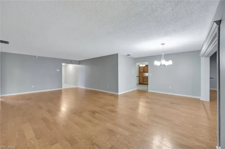 Unfurnished living room with a chandelier, a textured ceiling, and light wood-type flooring