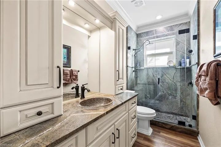 Full bath featuring vanity, a marble finish shower, ornamental molding, and dark wood finished floors