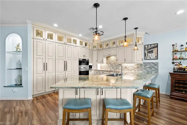 Kitchen featuring crown molding, a peninsula, light stone counters, a breakfast bar, and dark wood-style flooring