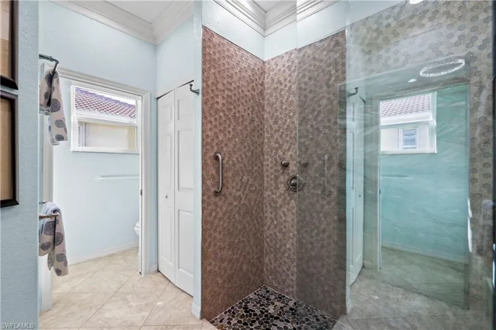 Bathroom featuring ornamental molding, a shower stall, a closet, and light tile patterned flooring