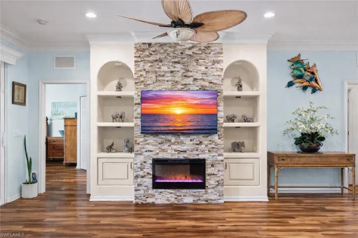 Living room featuring built in features, crown molding, dark wood-type flooring, a fireplace, and a ceiling fan