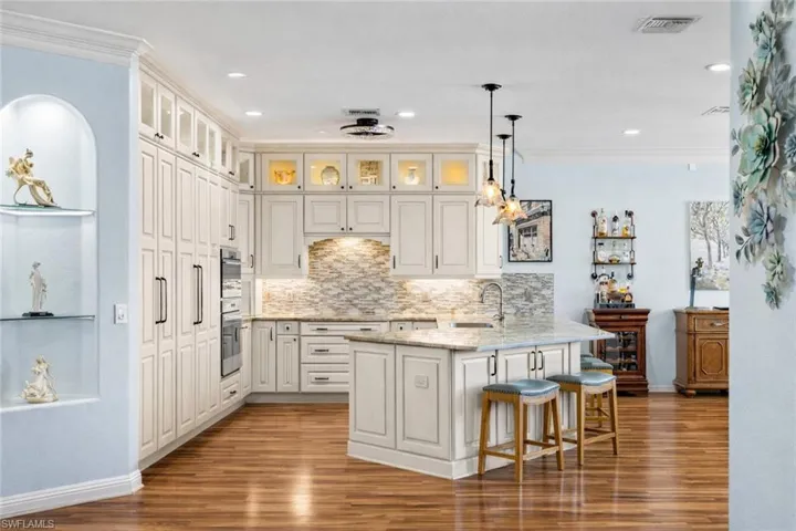Kitchen with hanging light fixtures, light stone countertops, a kitchen breakfast bar, light wood-style floors, and ornamental molding