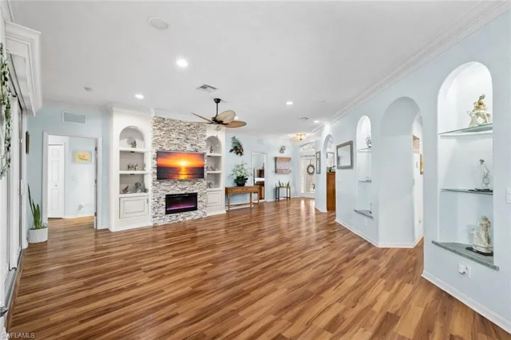 Unfurnished living room with built in shelves, ceiling fan, a fireplace, ornamental molding, and wood finished floors