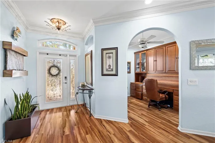 Entryway with crown molding, light wood-style floors, arched walkways, and a ceiling fan