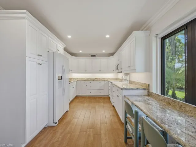 Kitchen featuring white appliances, white cabinets, light wood-type flooring, light stone counters, and ornamental molding