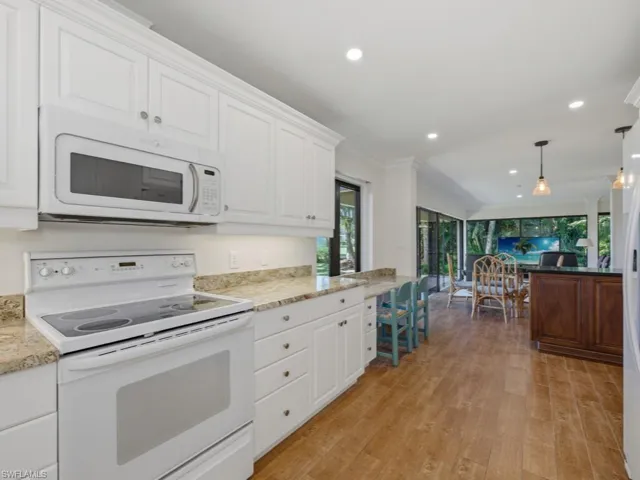 Kitchen featuring white appliances, hanging light fixtures, light stone counters, white cabinetry, and light wood finished floors