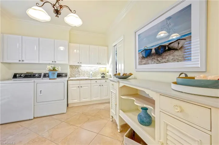 Washroom featuring cabinets, light tile patterned floors, crown molding, sink, and washing machine and dryer
