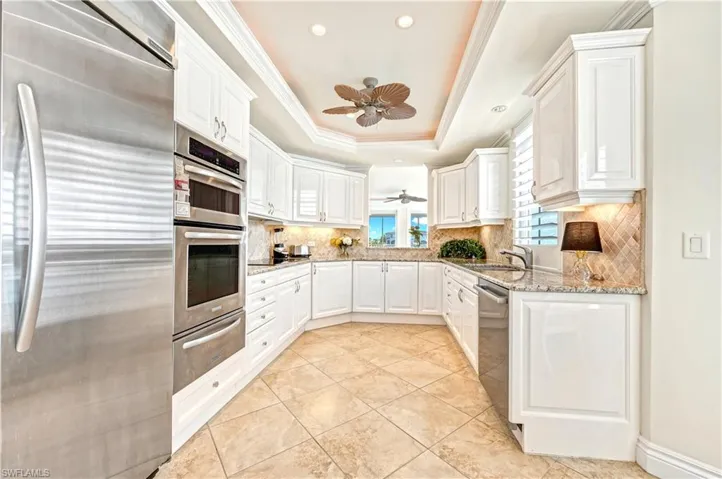 Kitchen featuring white cabinets, appliances with stainless steel finishes, a tray ceiling, and ceiling fan