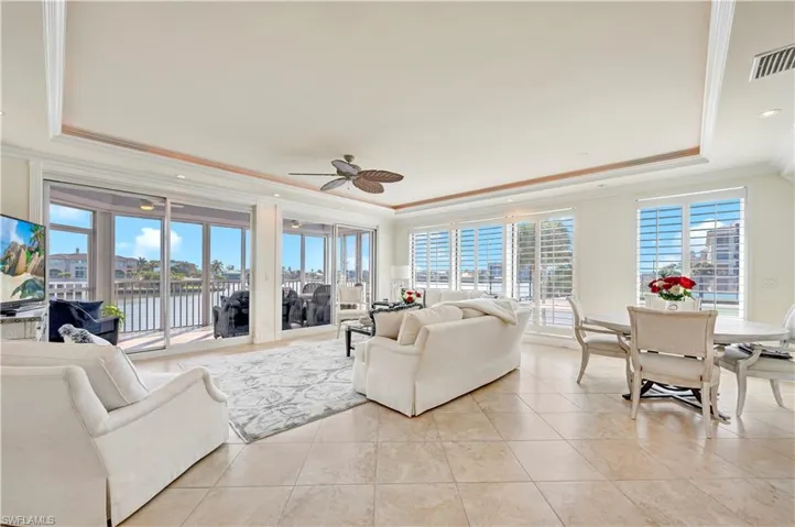 Tiled living room with a water view, ceiling fan, a raised ceiling, and crown molding