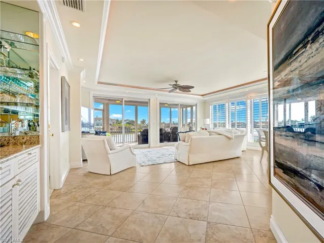 Tiled living room featuring a tray ceiling, crown molding, and ceiling fan