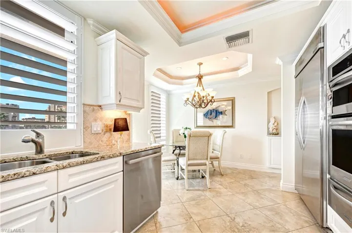 Kitchen with crown molding, sink, light stone countertops, a raised ceiling, and appliances with stainless steel finishes