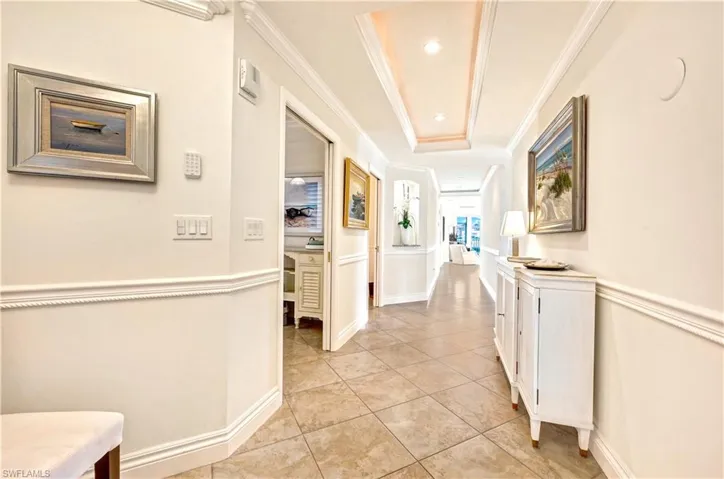Corridor featuring ornamental molding, a raised ceiling, and light tile patterned flooring