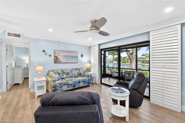 Living area featuring wood-finish flooring, a contemporary ceiling fan, and sliding glass doors with white louvered shutters