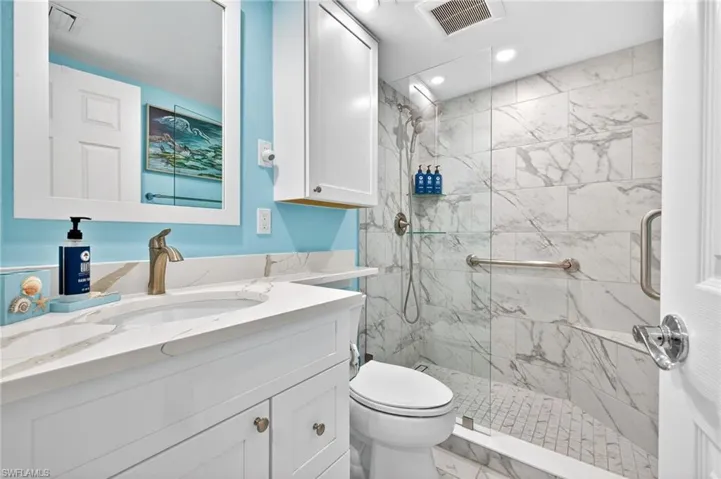Bathroom featuring a white vanity with a quartz countertop and an undermount sink, a bronze-finish faucet, a mirrored medicine cabinet, a tiled walk-in shower with a glass enclosure, and recessed lighting