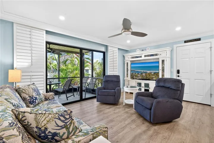 Living area featuring wood-finish flooring, a white ceiling fan, recessed lighting, and a white entry door