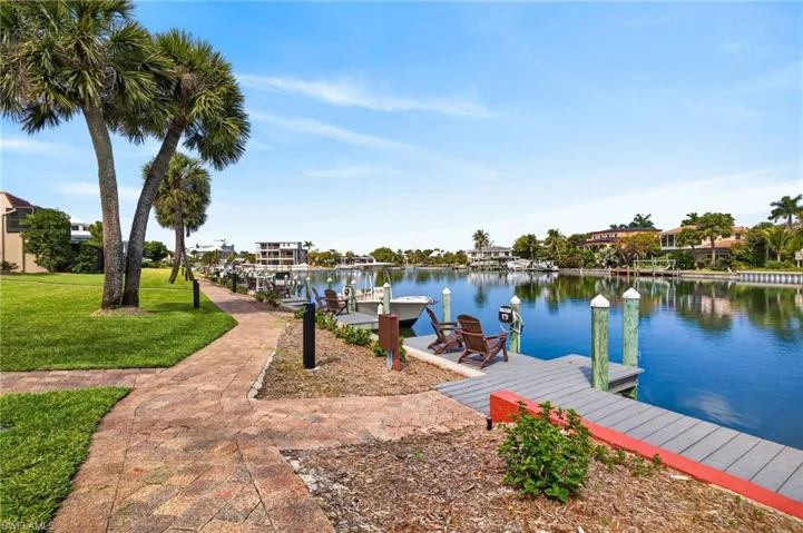 Waterfront property featuring a community dock with pilings, a paved pedestrian pathway, and mature palm trees