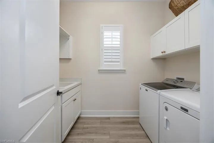 Laundry room with full size washer/dryer, plantation shutters, additional cabinet space, a laundry sink and hanging area above the sink