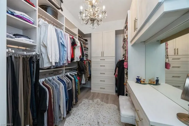 Walk in closet featuring custom closet system, light wood-type flooring and a custom chandelier