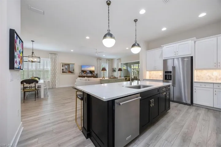 Upgraded Kitchen featuring custom lighting, quartz countertops, marble backsplash, white cabinetry, contrasting center island, cooktop, wall oven and under cabinet range hood