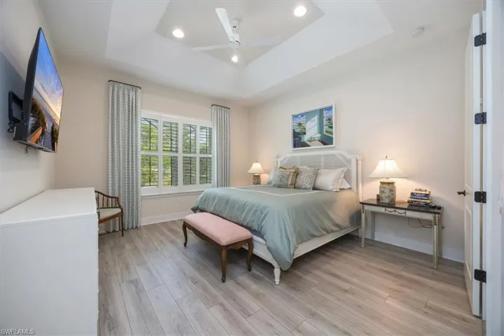 Primary Bedroom featuring light wood-style flooring, a tray ceiling, recessed lighting, custom drapery panels and plantation shutters