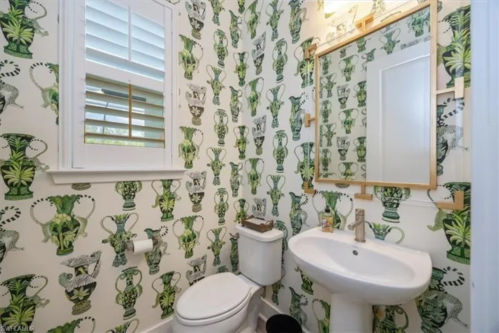 Half bath is located adjacent to the pool entrance and has custom wallpaper and plantation shutters