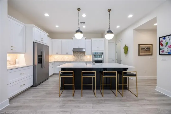 Upgraded Kitchen featuring custom lighting, quartz countertops, marble backsplash, white cabinetry, contrasting center island, cooktop, wall oven and under cabinet range hood