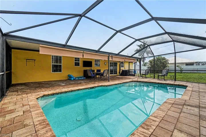 Screened-in swimming pool enclosure featuring a rectangular pool, brick paver decking, and a covered lanai