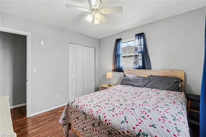 Bedroom featuring wood-finish flooring, a ceiling fan with integrated lighting, a window with horizontal blinds, and bi-fold closet doors