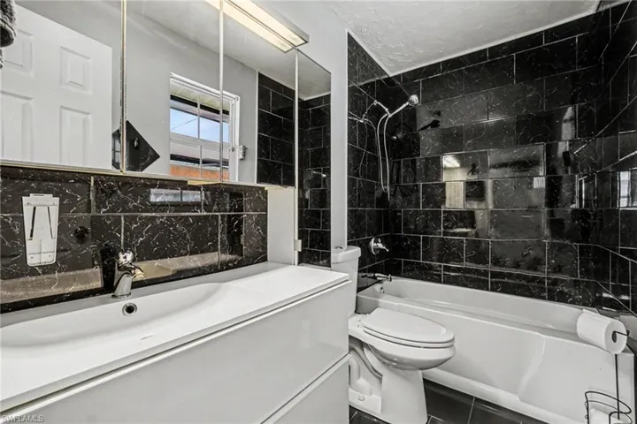 Black marble-effect tiled bathroom featuring a white vanity with integrated sink, chrome faucet, and a large mirrored medicine cabinet