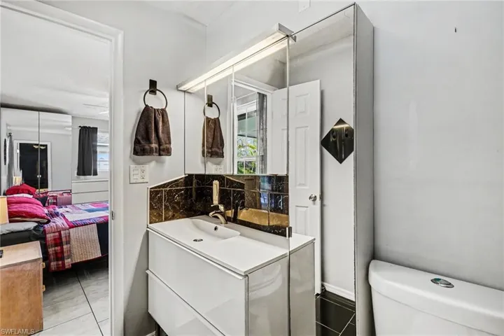 Bathroom vanity featuring a white rectangular sink with a single-handle faucet, dark tile backsplash, and a large mirrored medicine cabinet with integrated lighting