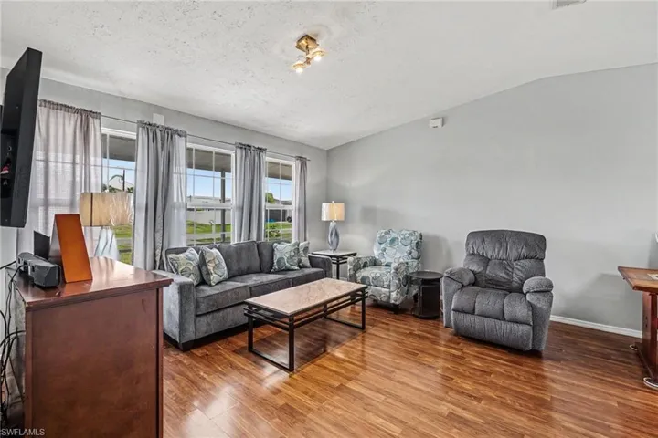 Interior living space featuring wood-finish flooring, light gray wall paint, and multiple windows with vertical blinds