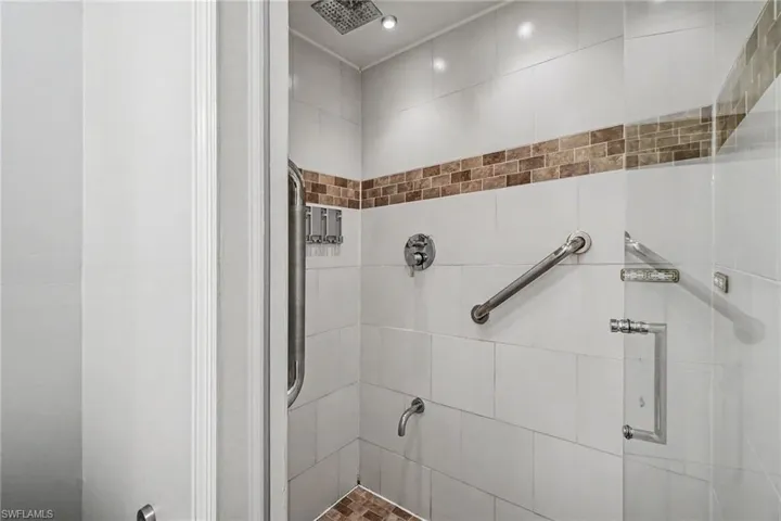 Walk-in shower featuring white tile walls with a decorative brown accent band and a coordinated brown tile floor