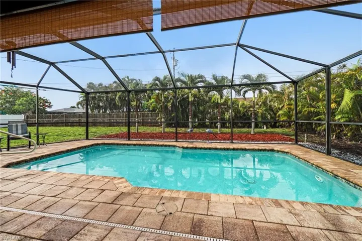 Screened-in outdoor pool featuring a paver deck, surrounding landscaping, and mature palm trees