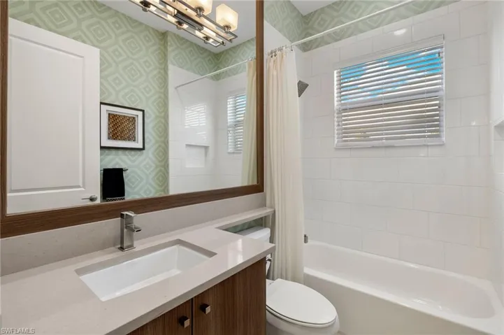 Bathroom with vanity, shower / bathtub combination with curtain, toilet, and wallpapered walls