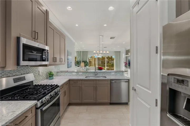 Kitchen with stainless steel appliances, a sink, visible vents, backsplash, and light stone countertops