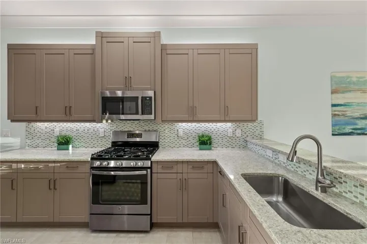 Kitchen with light stone counters, decorative backsplash, stainless steel appliances, and a sink