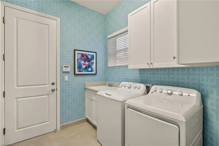 Laundry area with a sink, baseboards, independent washer and dryer, cabinet space, and wallpapered walls