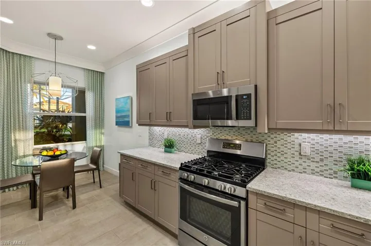 Kitchen featuring appliances with stainless steel finishes, light stone countertops, pendant lighting, and tasteful backsplash