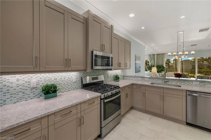 Kitchen with a sink, visible vents, appliances with stainless steel finishes, decorative backsplash, and light stone countertops