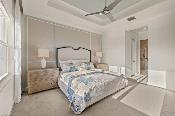 Bedroom with ceiling fan, a raised ceiling, visible vents, and light colored carpet