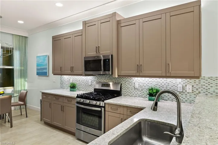 Kitchen with light stone counters, appliances with stainless steel finishes, decorative backsplash, and a sink